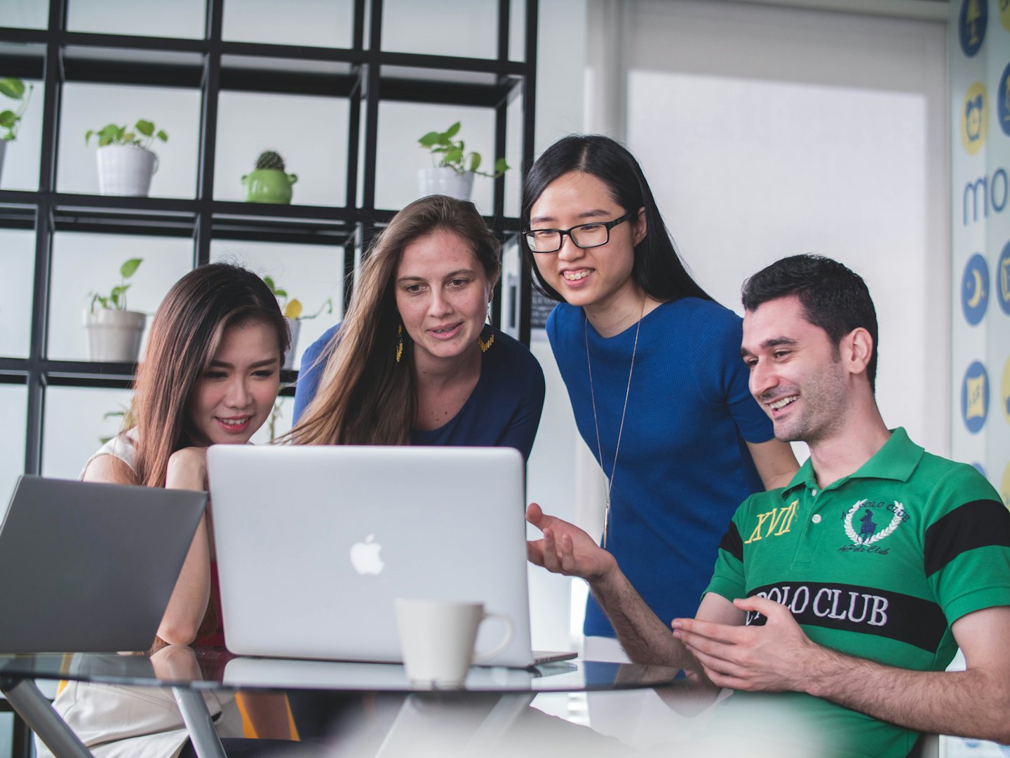 Vier diverse professionals werken samen rond een laptop in een modern kantoor.